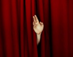 Hand waving from behind a theater curtain. Illustrates how to overcome shyness