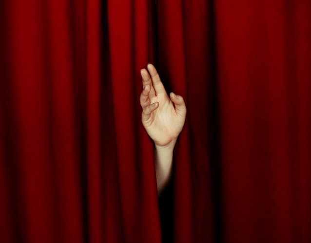 Hand waving from behind a theater curtain. Illustrates how to overcome shyness